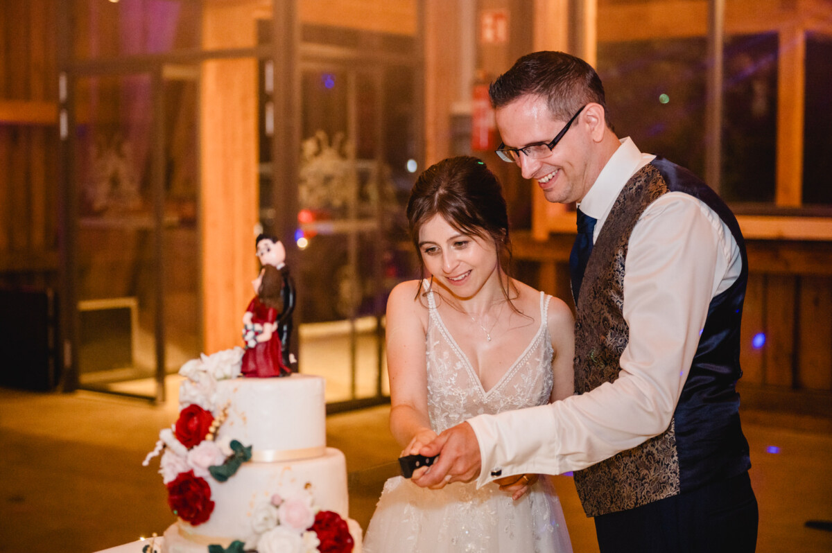 Ein Paar schneidet eine mehrstöckige Hochzeitstorte an, die mit roten und weißen Blumen geschmückt ist.