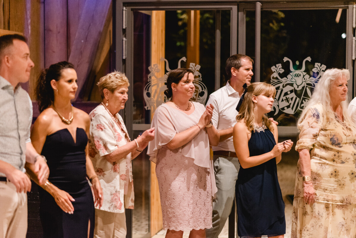 Eine Gruppe von Menschen in Abendgarderobe steht in einem Innenbereich zusammen, klatscht und beobachtet etwas außerhalb des Kamerablickfelds.