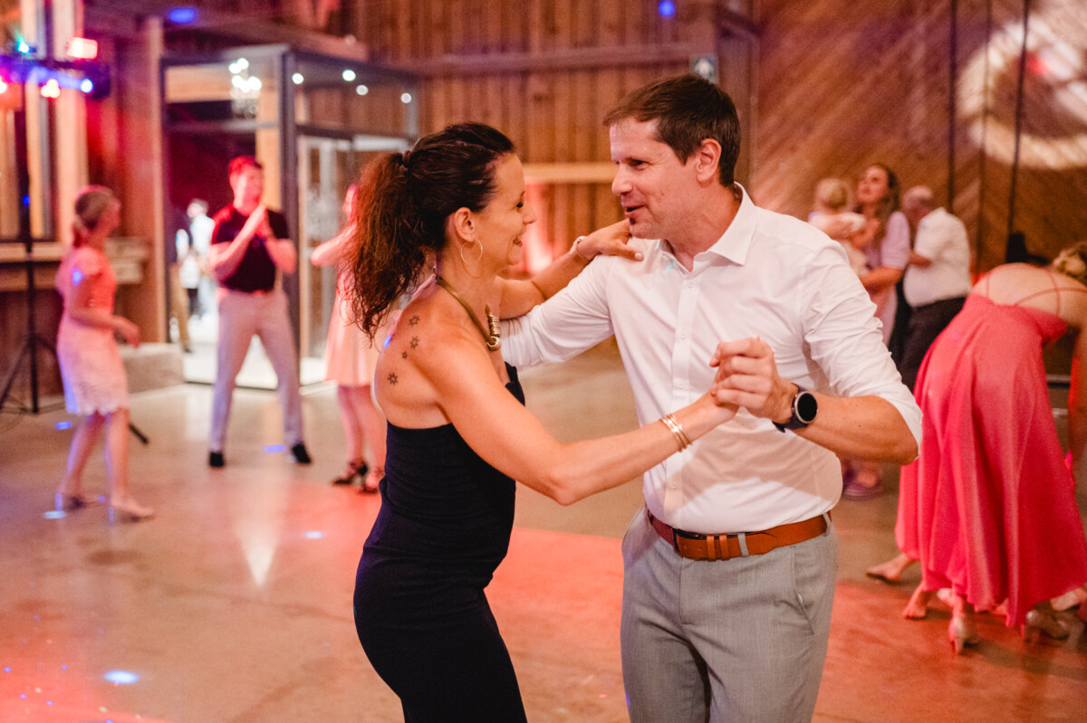 Ein Mann und eine Frau tanzen fröhlich auf einer lebhaften Indoor-Party, umgeben von anderen Gästen in festlicher Kleidung.