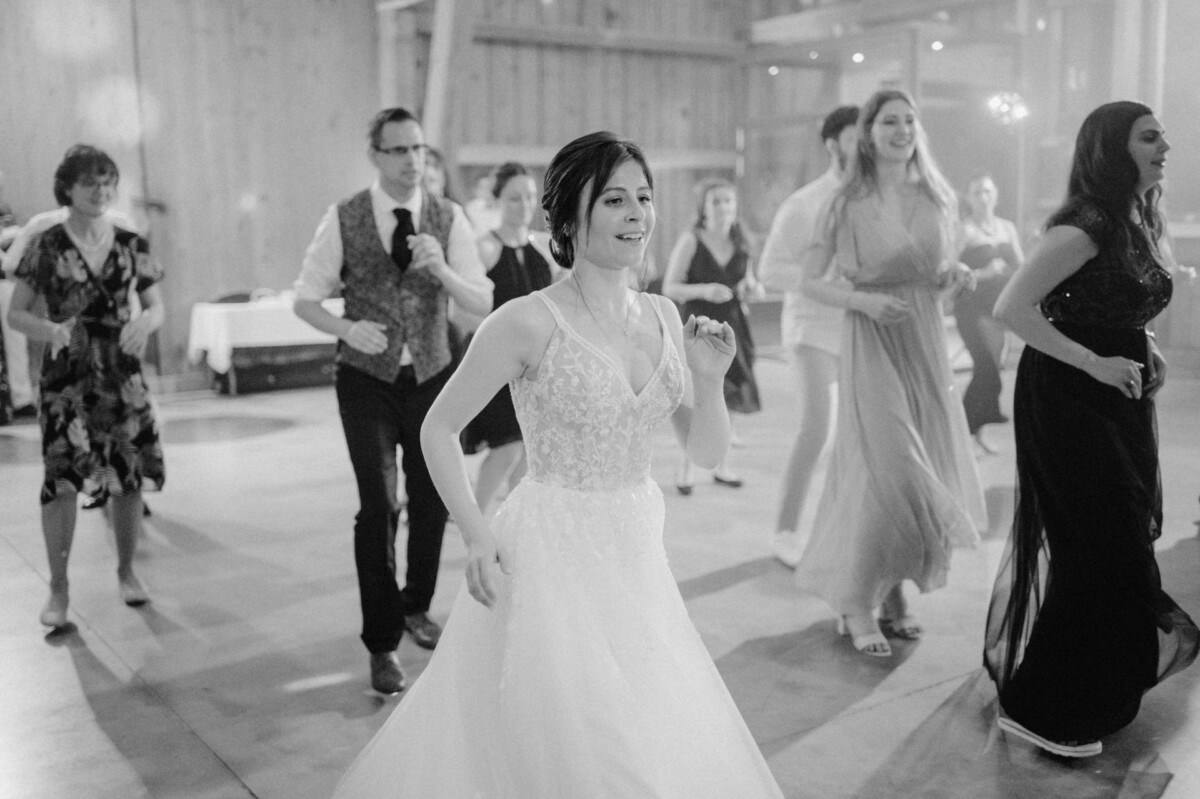 Eine Braut im Hochzeitskleid tanzt mit Gästen in einem rustikalen Veranstaltungsort.