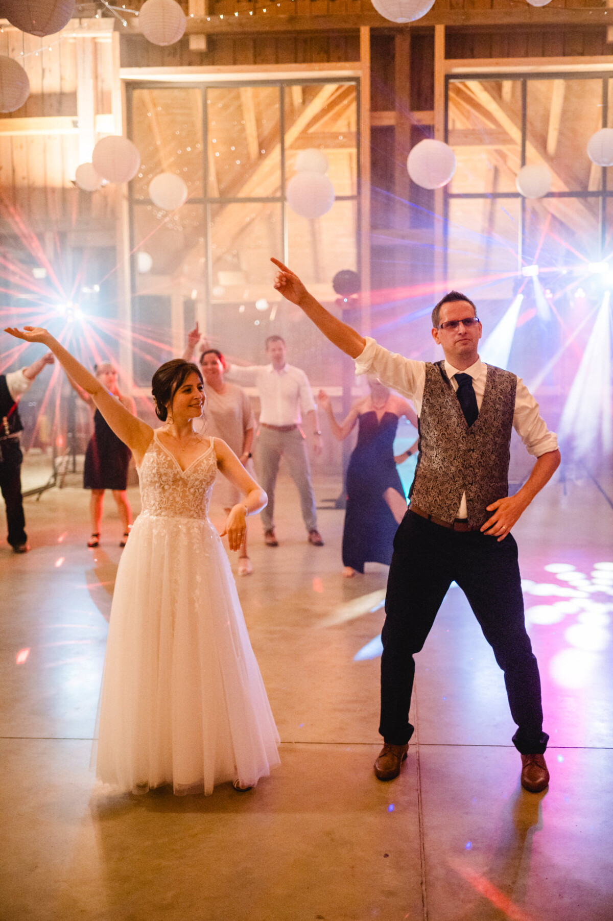 Eine Braut und ein Bräutigam tanzen bei einer Hochzeitsfeier, im Hintergrund sind Gäste zu sehen.