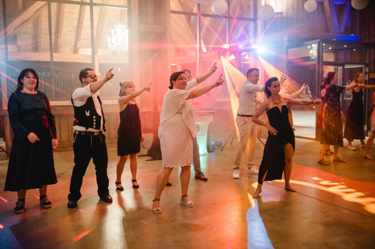 Eine Gruppe von Menschen auf einer Tanzfläche, die in die gleiche Richtung zeigen, wobei bunte Lichter die Szene beleuchten.