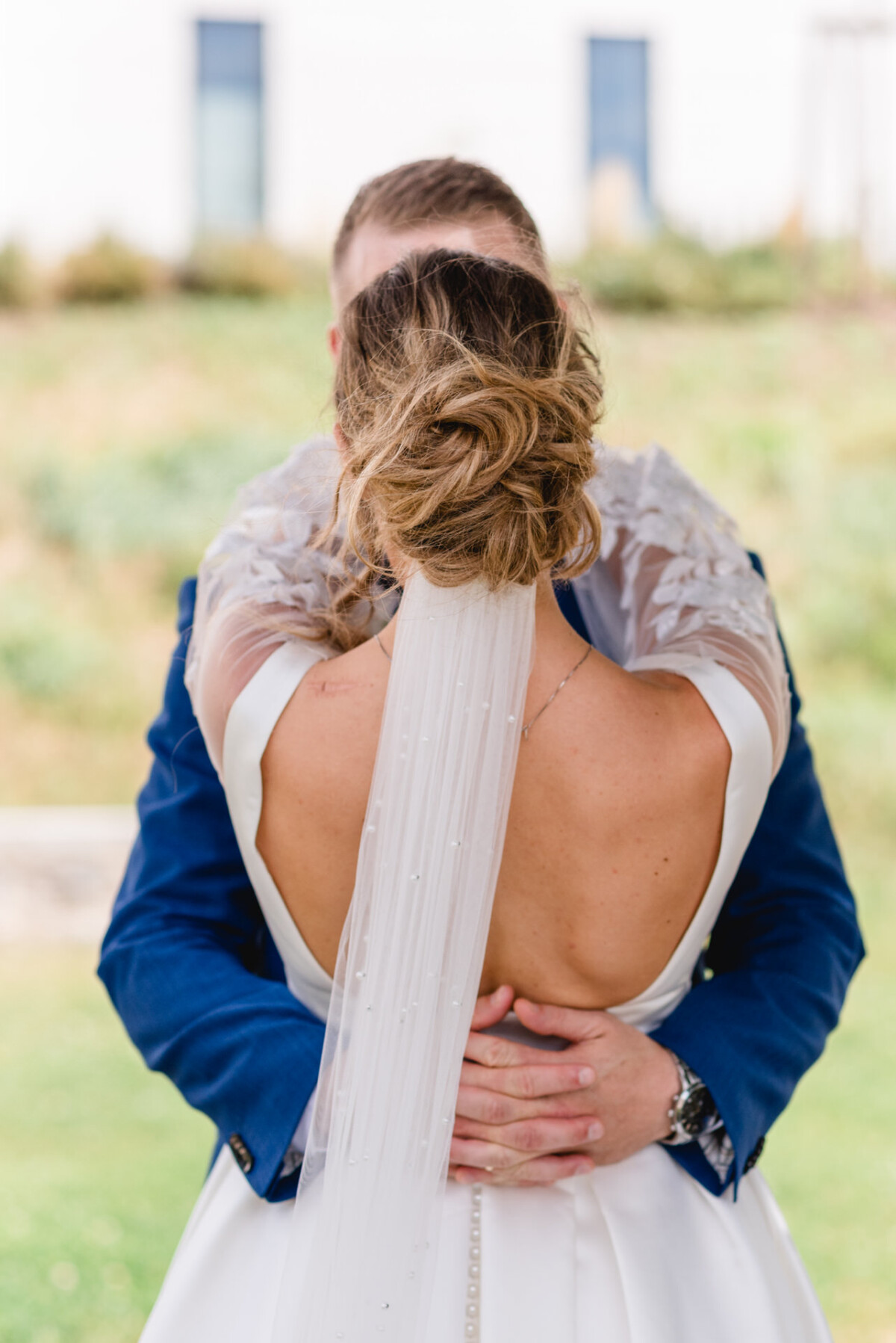 Braut und Bräutigam umarmen sich einander zugewandt. Der Fokus liegt auf dem Rücken der Braut, der ihre Frisur und ihren Schleier zeigt.