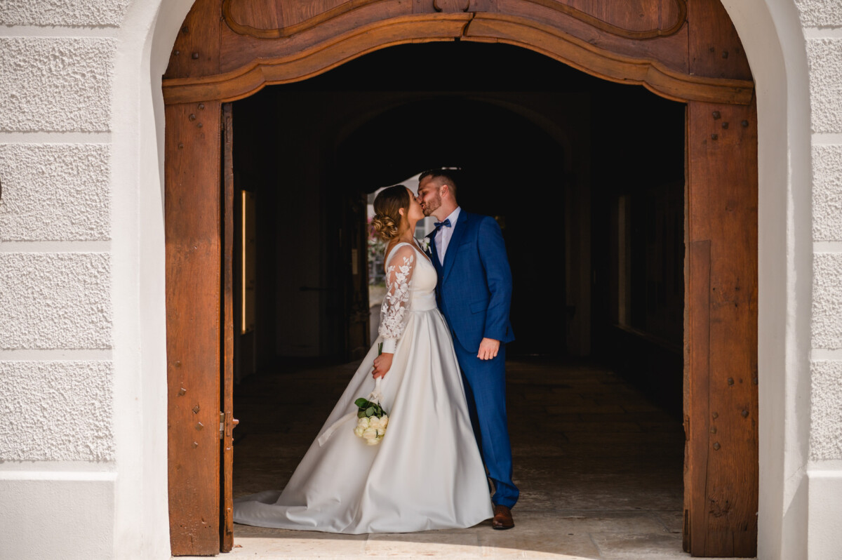 Braut und Bräutigam stehen unter einem Torbogen, die Braut hält einen Blumenstrauß.