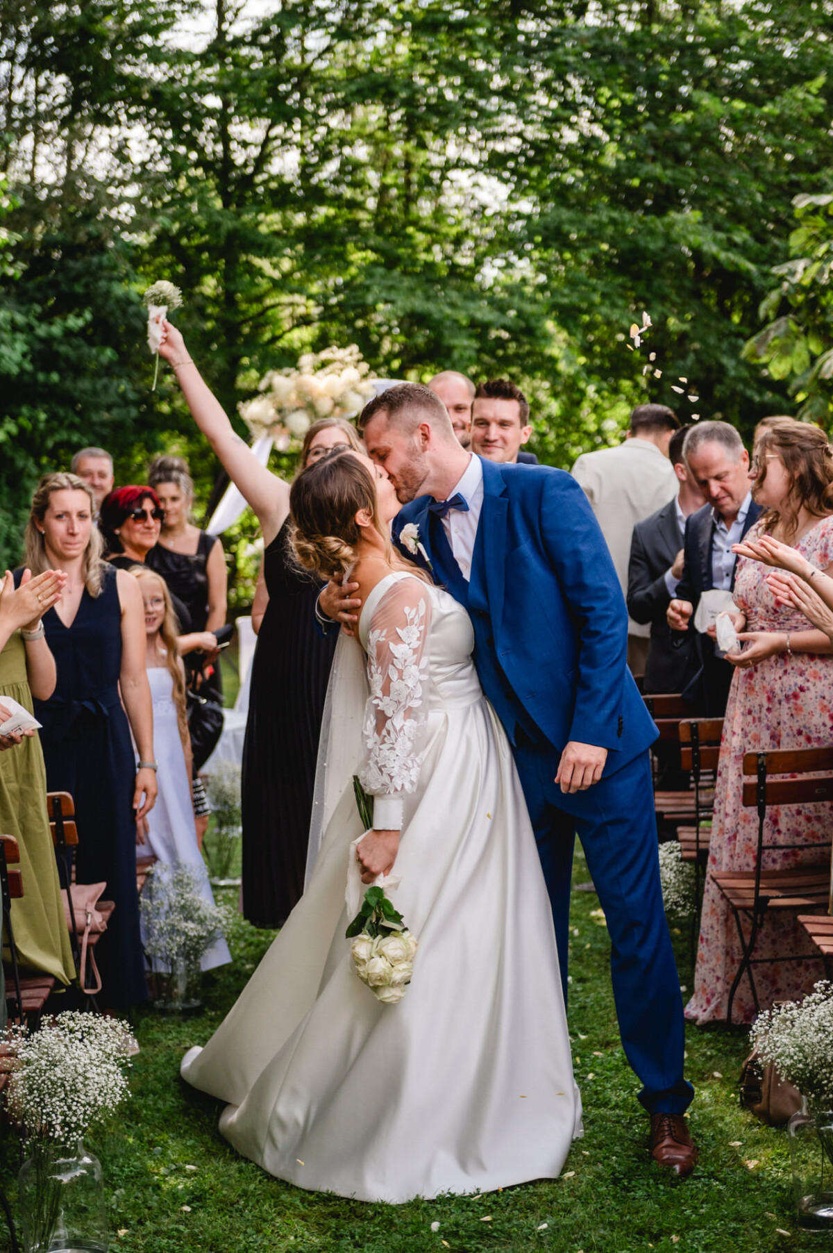 Braut und Bräutigam küssen sich bei einer Hochzeitszeremonie im Freien, umgeben von Gästen.