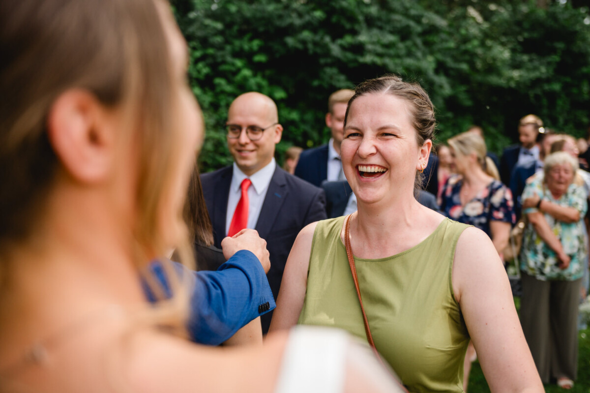 Eine Frau in einem grünen Kleid lächelt und unterhält sich mit anderen draußen, umgeben von Menschen in Abendgarderobe.