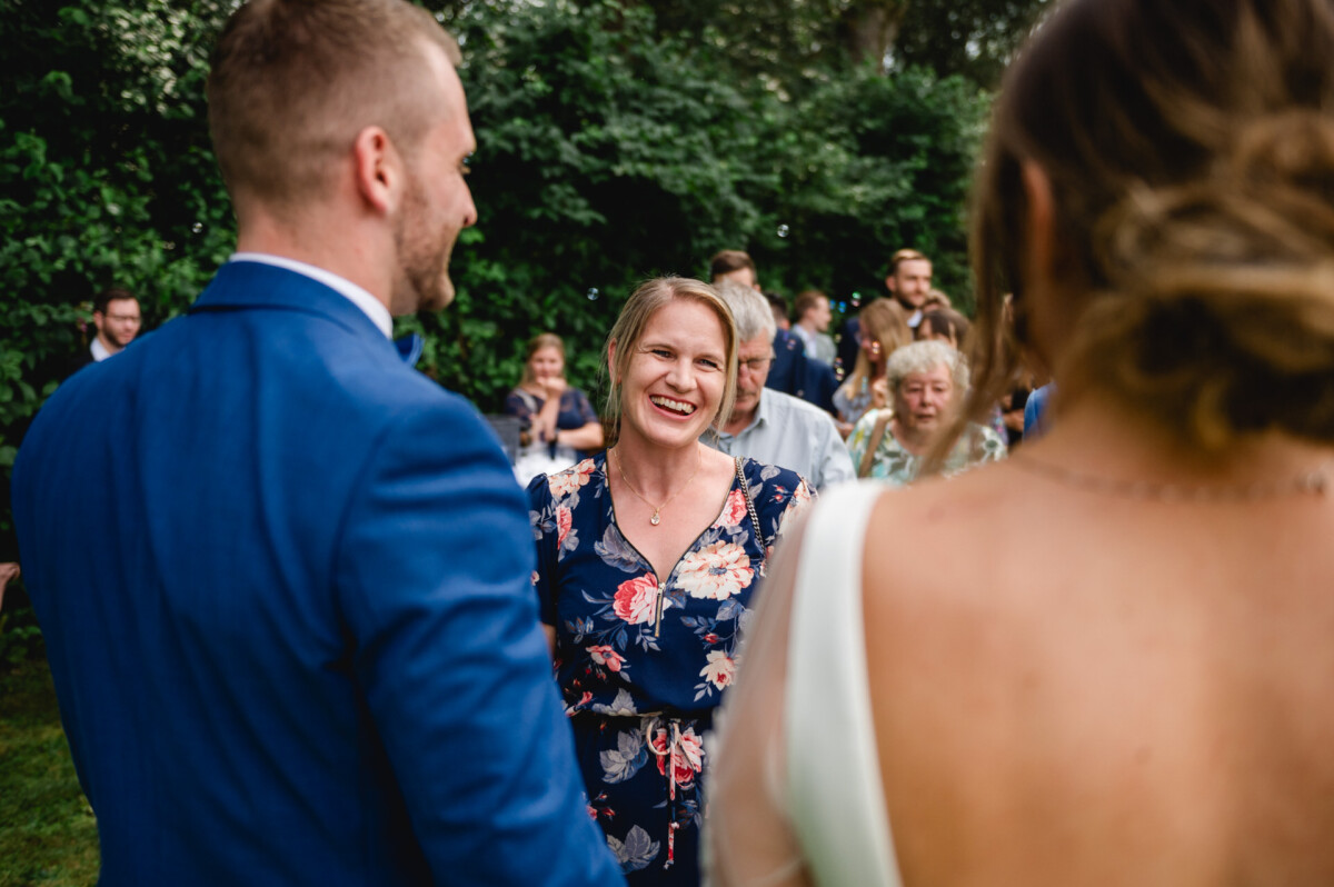 Eine Frau in einem geblümten Kleid lächelt, während sie bei einer Versammlung im Freien mit einem Mann in einem blauen Anzug und einer Frau in einem weißen Kleid spricht.