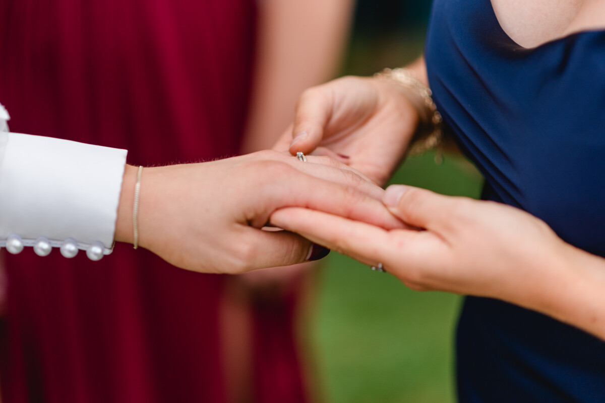 Während einer Zeremonie steckt eine Person einer anderen Person einen Ring an den Finger.