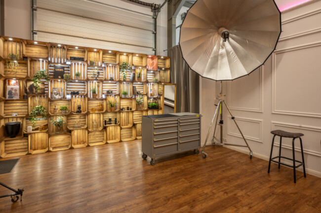 Fotostudio mit großer Lampe, Hocker und Rollwagen. Holzboden und Wanddisplay mit Pflanzen und Dekor.