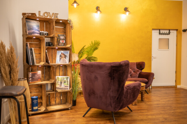 Gemütliches Zimmer mit lila Stühlen, einem Holzregal mit Büchern und Dekorationen mit der Aufschrift „LOVE“ und einer gelben Wand mit drei Lichtern.