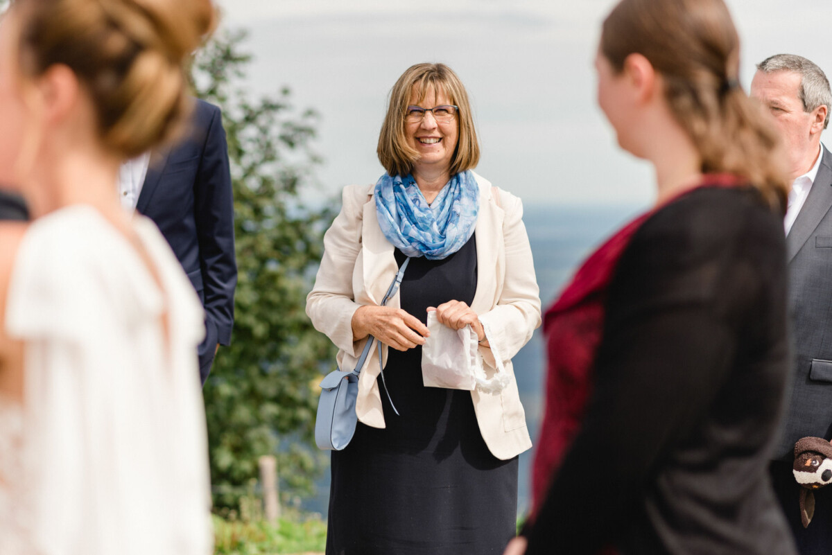 Eine Frau mit blauem Schal und Brille lächelt bei einer Versammlung im Freien, umgeben von Menschen.