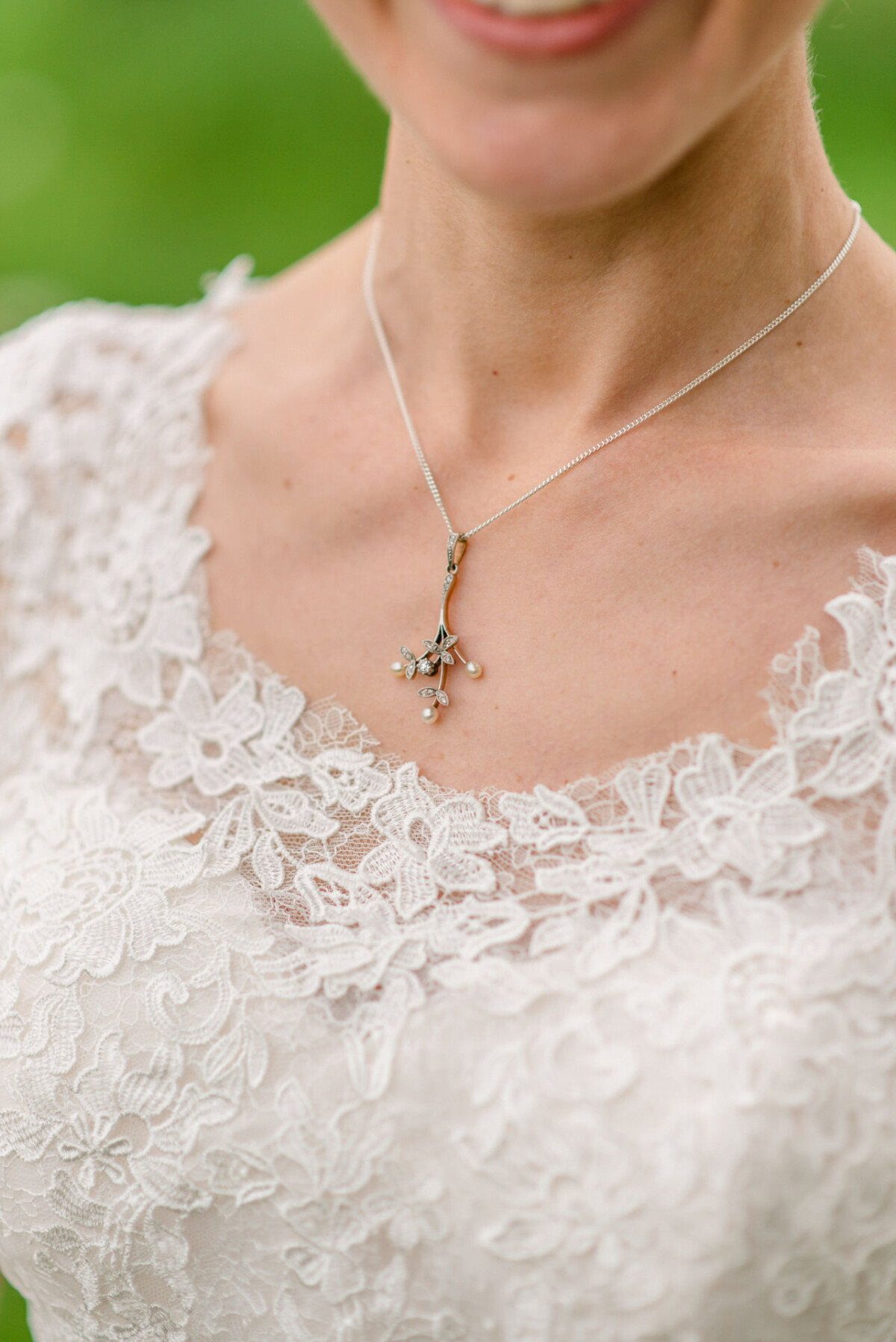 Nahaufnahme einer Frau, die ein zartes Spitzenkleid und eine Halskette mit floralem Anhänger trägt.