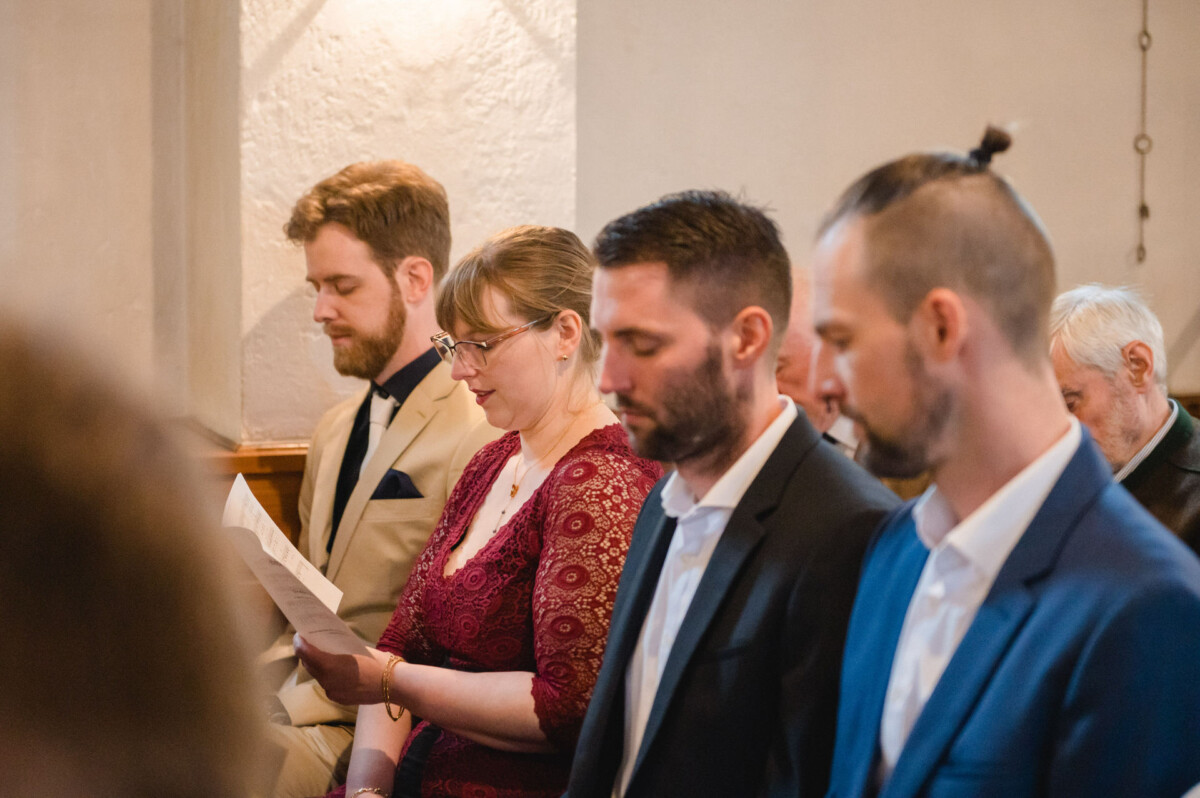 Vier Personen in formeller Kleidung stehen nebeneinander in einem Raum, wobei eine Person ein Stück Papier hält.