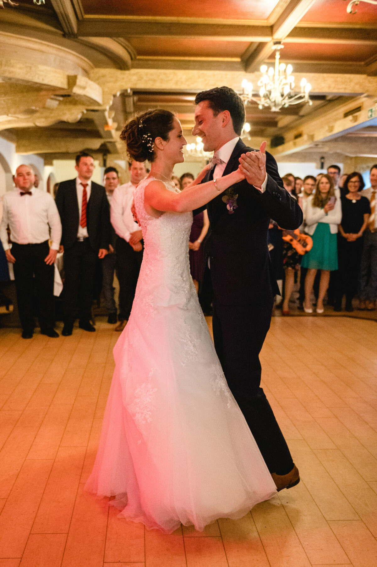 Braut und Bräutigam tanzen gemeinsam auf einem Holzboden, während die Menge zusieht.