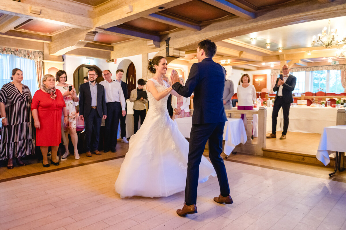 Ein Paar tanzt im Hochzeitskleid in einem Bankettsaal, umgeben von zuschauenden und klatschenden Gästen.