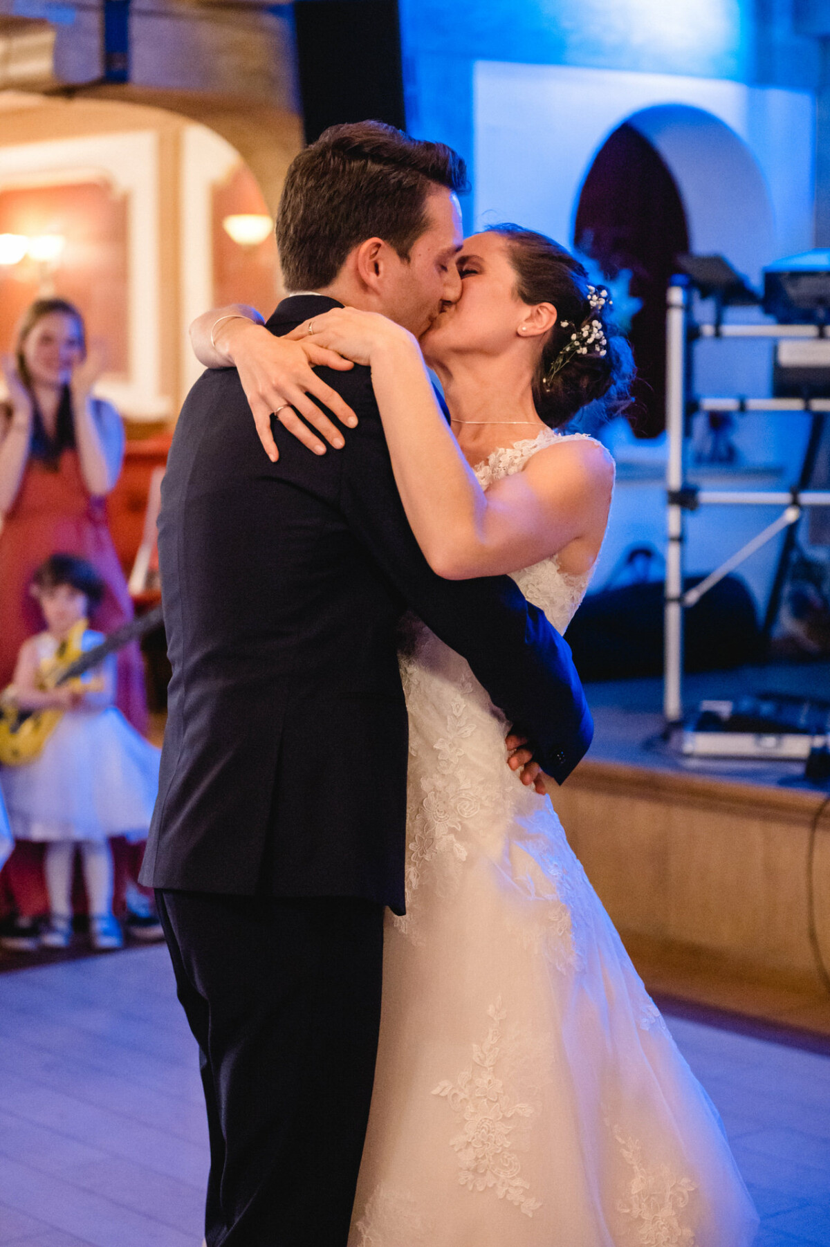 Braut und Bräutigam küssen sich bei ihrer Hochzeit auf der Tanzfläche, während die Gäste im Hintergrund zuschauen.