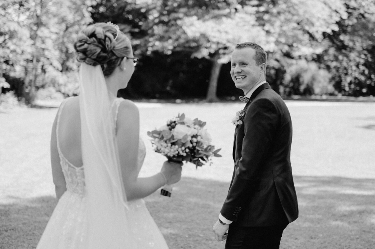 Braut und Bräutigam lächeln sich im Freien an, die Braut hält einen Blumenstrauß. Schwarzweißbild.