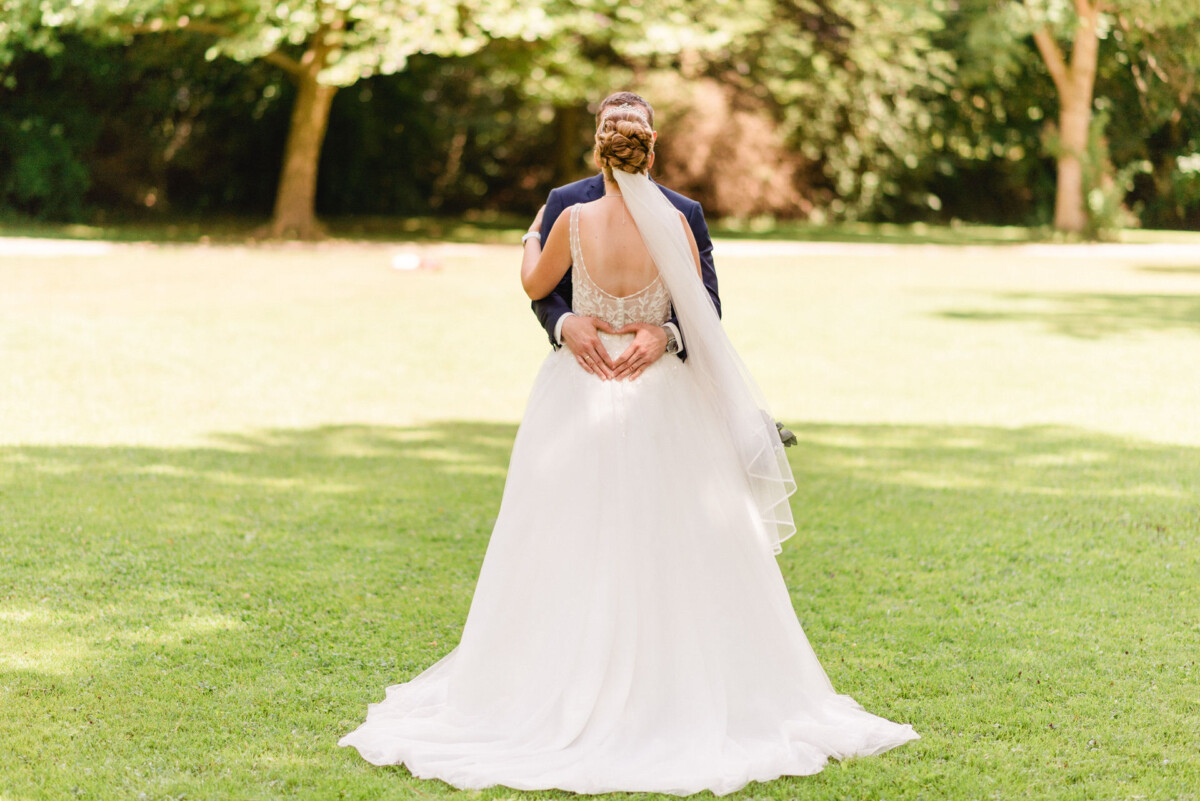 Braut und Bräutigam umarmen sich auf einer Wiese mit Bäumen im Hintergrund.