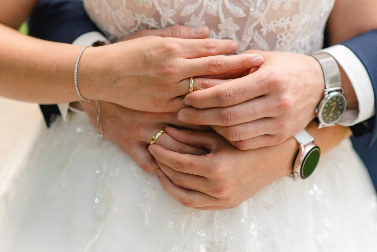 Ein Paar im Hochzeitskleid hält sich gegenseitig und zeigt seine Eheringe und Uhren an ihren Handgelenken.