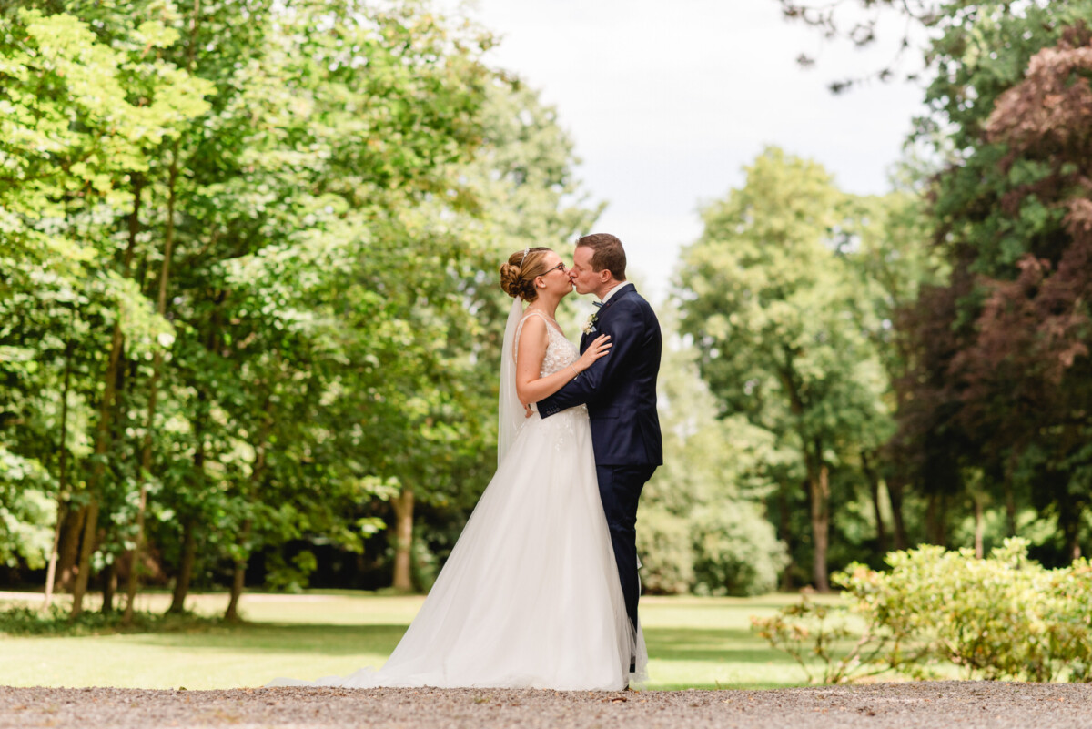 Braut und Bräutigam küssen sich in einem üppig grünen Park, umgeben von Bäumen und Grün.