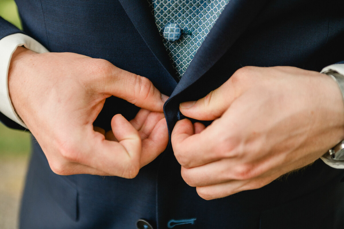 Person knöpft ein dunkelblaues Jackett über einer gemusterten blauen Krawatte zu.