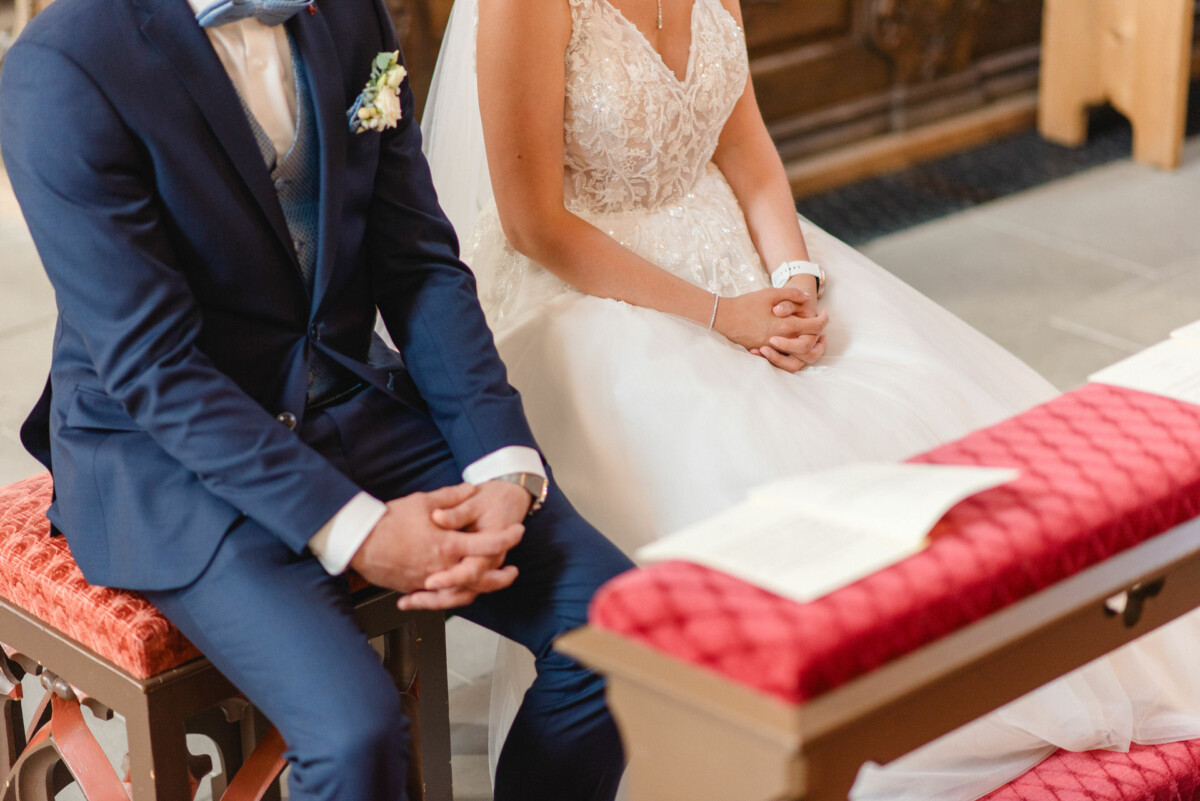 Ein Paar in Abendgarderobe sitzt während einer Zeremonie Seite an Seite auf rot gepolsterten Bänken.
