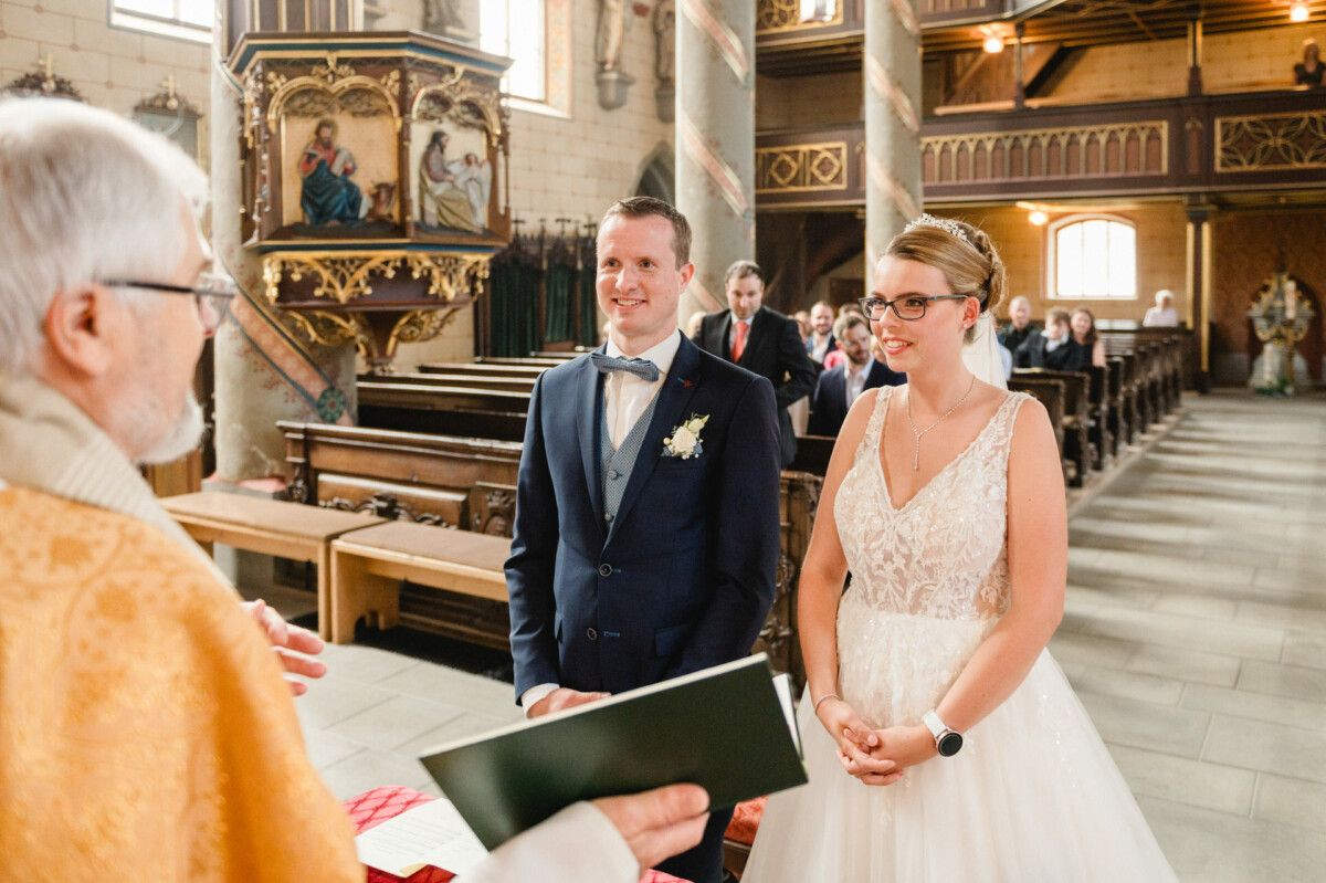 Braut und Bräutigam stehen gemeinsam in einer Kirche und stehen einem Geistlichen gegenüber, der eine Trauungszeremonie durchführt.