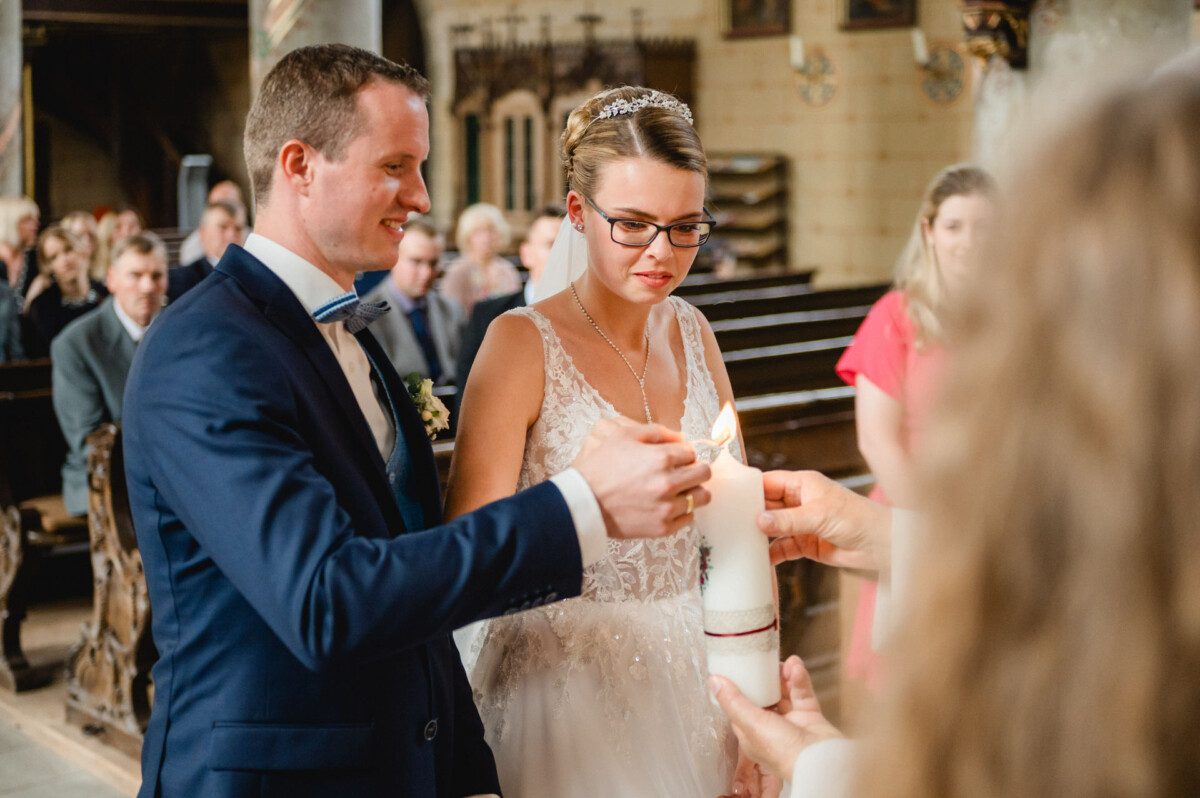Braut und Bräutigam zünden während ihrer Hochzeitszeremonie gemeinsam eine Kerze an, während die Gäste im Hintergrund sitzen.