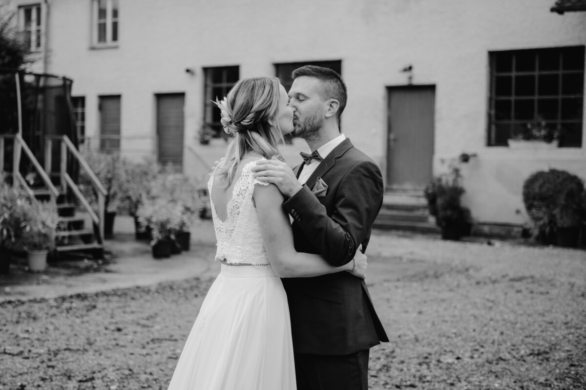 Ein Paar in Abendgarderobe küsst sich im Freien, im Hintergrund ist ein Gebäude zu sehen.