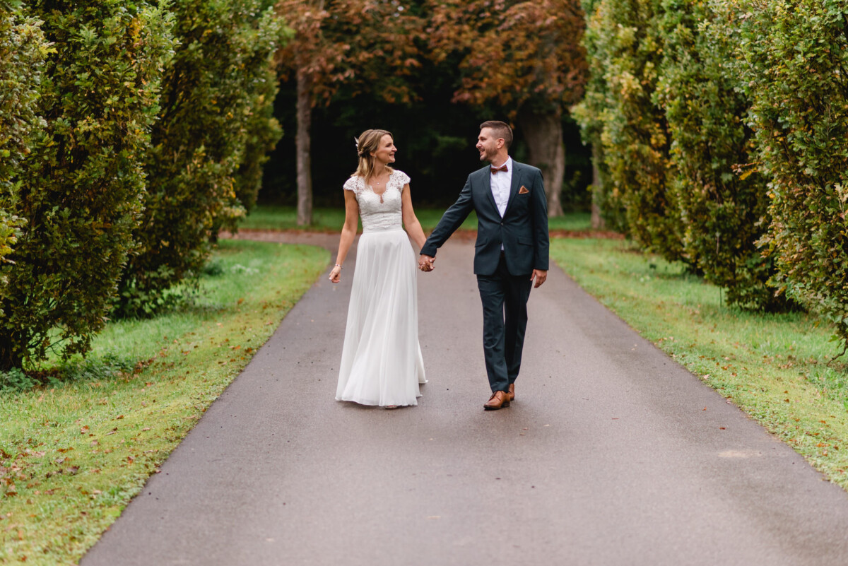 Ein Paar in Abendgarderobe geht Hand in Hand einen von Bäumen gesäumten Weg entlang.