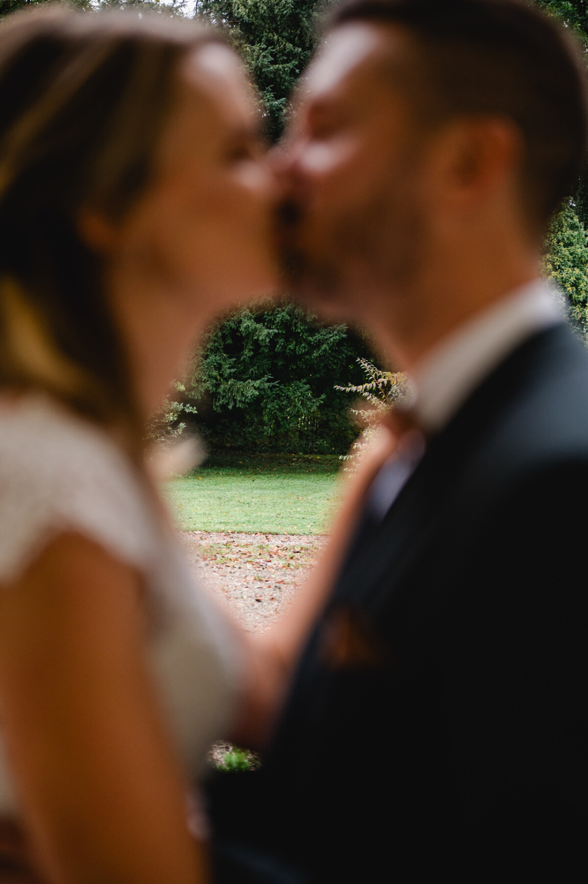 Ein paar Küsse im Freien mit Bäumen im Hintergrund, beides leicht unscharf.