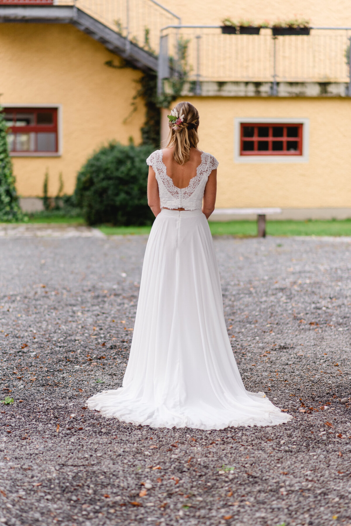 Eine Frau in einem weißen Brautkleid steht im Freien auf Kies und blickt von der Kamera weg.