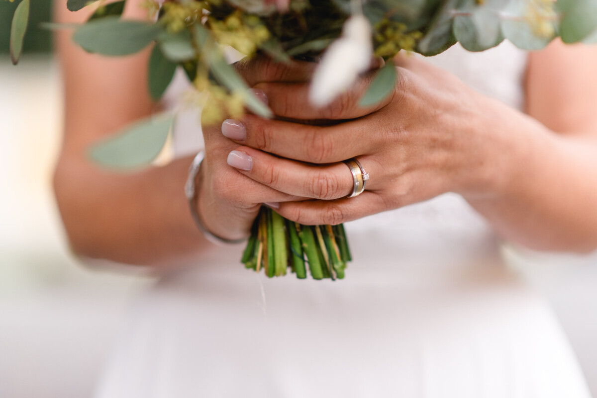 Braut hält einen Strauß grüner und weißer Blumen und trägt einen Ehering.