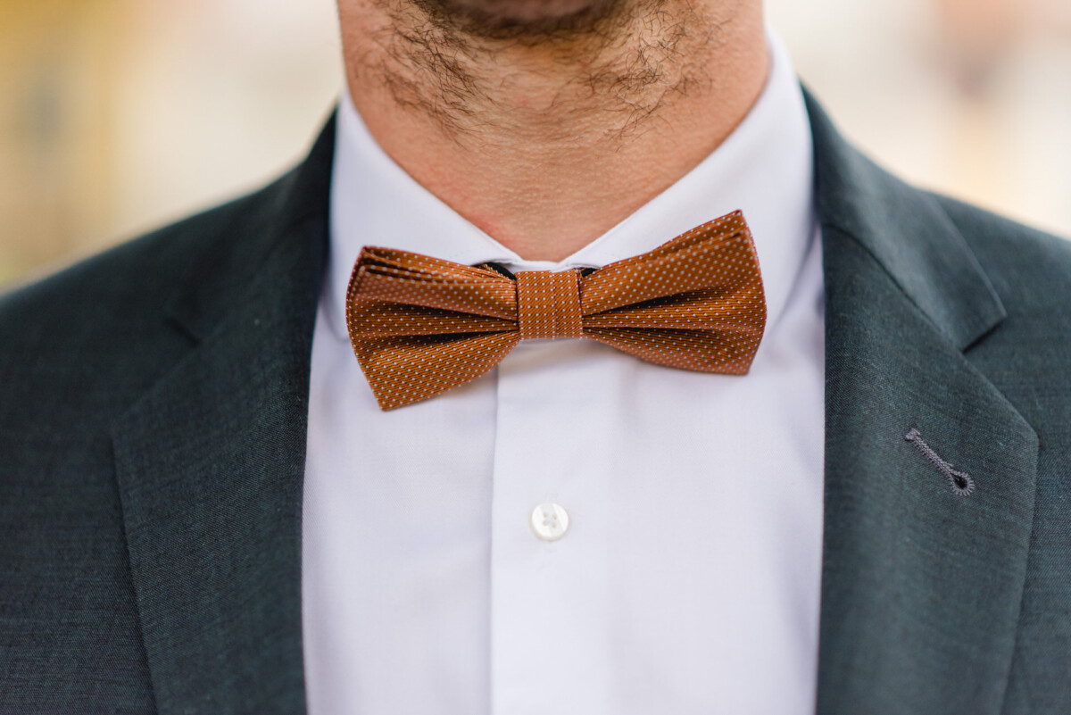 Ein Mann trägt einen dunklen Anzug und ein weißes Hemd mit einer braunen gepunkteten Fliege.