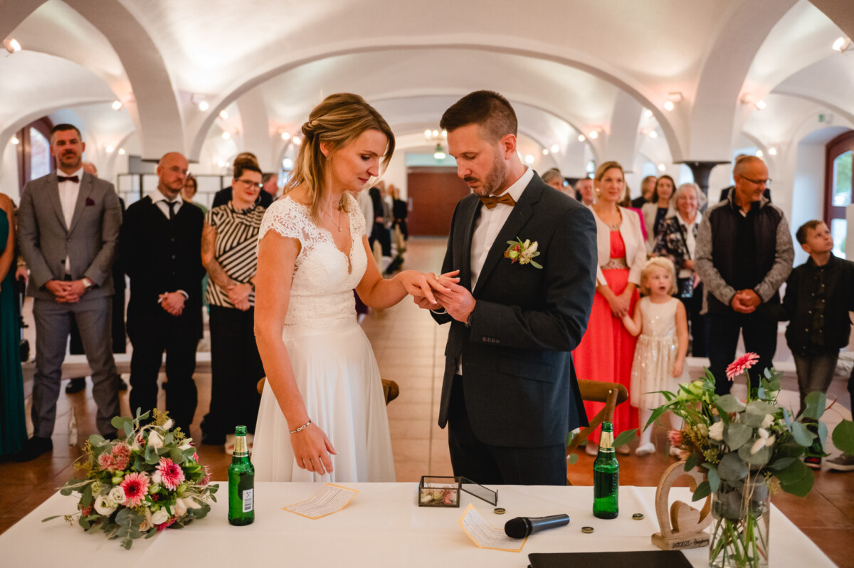Braut und Bräutigam tauschen während einer Hochzeitszeremonie in einem dekorierten Raum vor den Augen der Gäste Ringe aus.