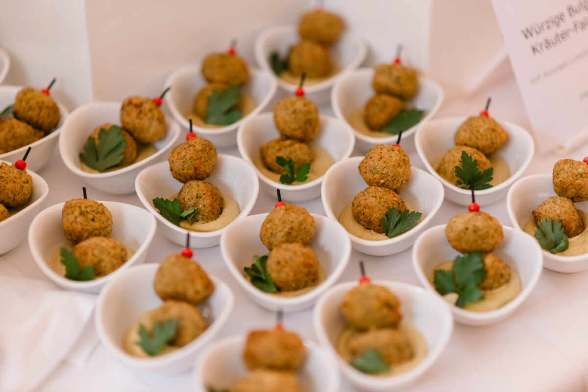 Kleine Schüsseln mit Falafel-Spießen, garniert mit Petersilie, auf einer weißen Oberfläche platziert.