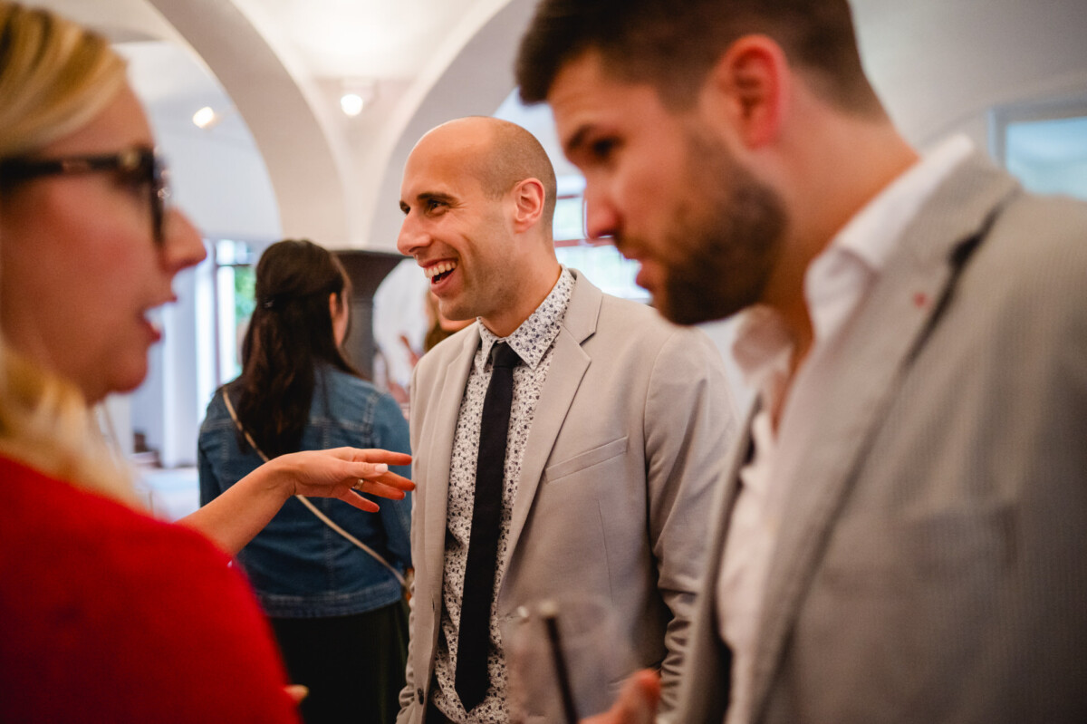 Menschen unterhalten sich bei einer gesellschaftlichen Veranstaltung, wobei eine lächelnde Person im Mittelpunkt steht.