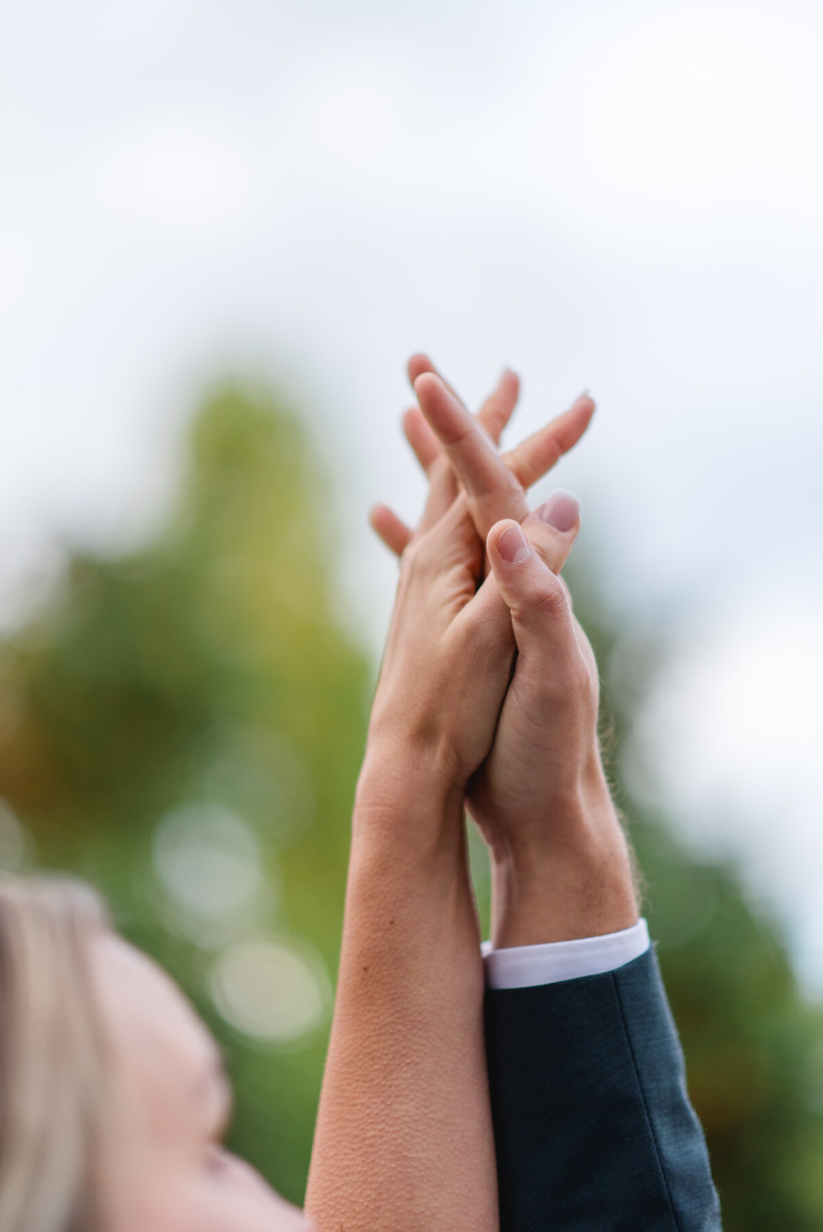 Zwei Personen heben ihre verschränkten Hände vor einem unscharfen Außenhintergrund.
