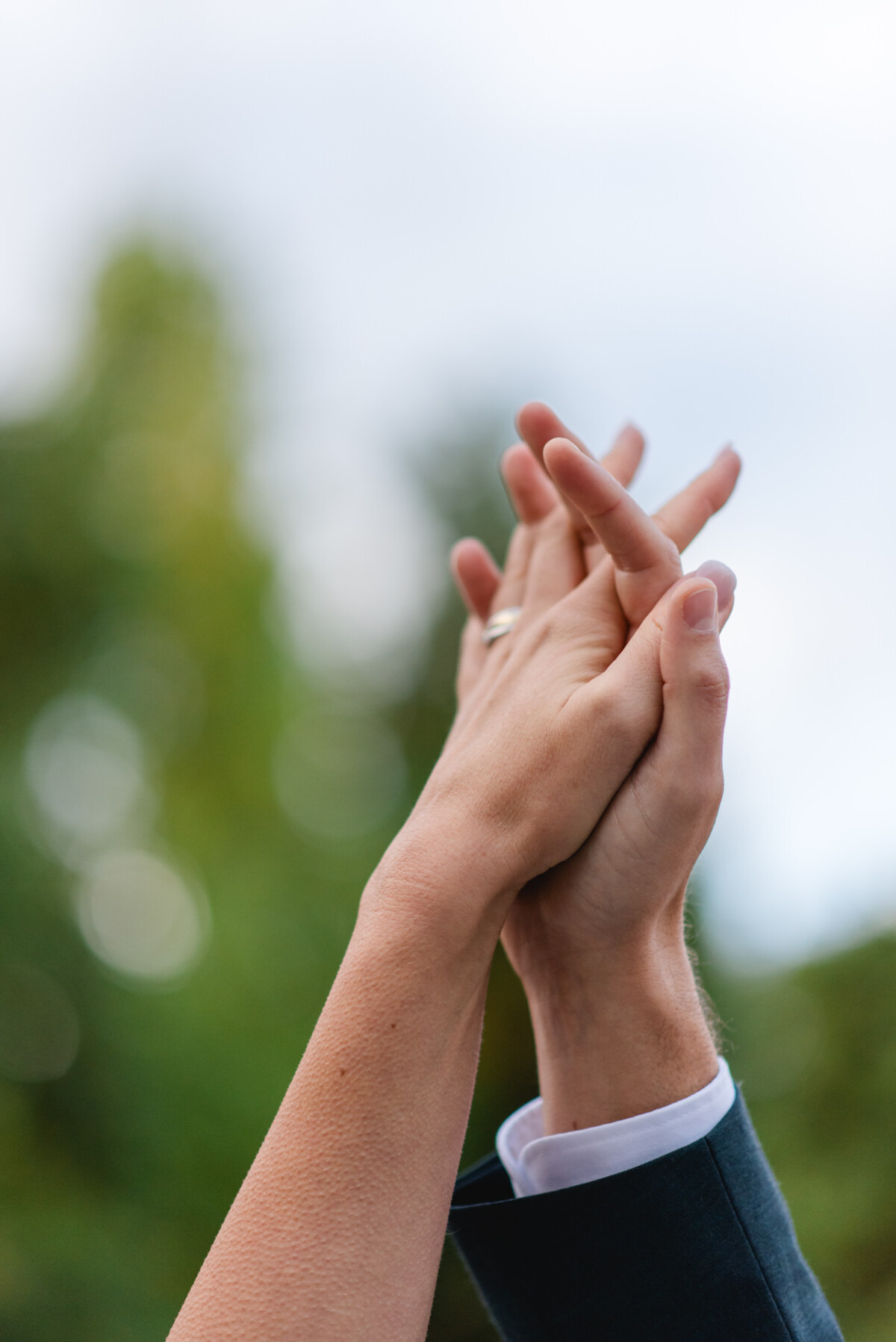 Zwei Menschen halten sich im Freien mit verschränkten Fingern an den Händen, vor einem unscharfen natürlichen Hintergrund.