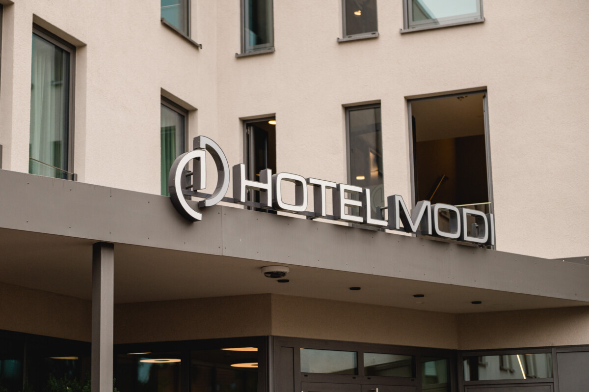 christian-lorenz.net Ein Schild mit der Aufschrift „Hotel Mod“ ziert die elegante Außenseite eines modernen Gebäudes, das an elegante Veranstaltungsorte wie Schloss Dachau erinnert und perfekt für alle ist, die in München nach einem einzigartigen Ambiente suchen.