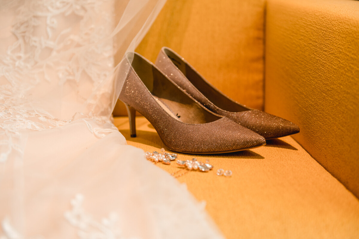 christian-lorenz.net Glitzernde Stöckelschuhe auf einem orangefarbenen Sofa, daneben ein Spitzenstoff und zarte Schmuckstücke.