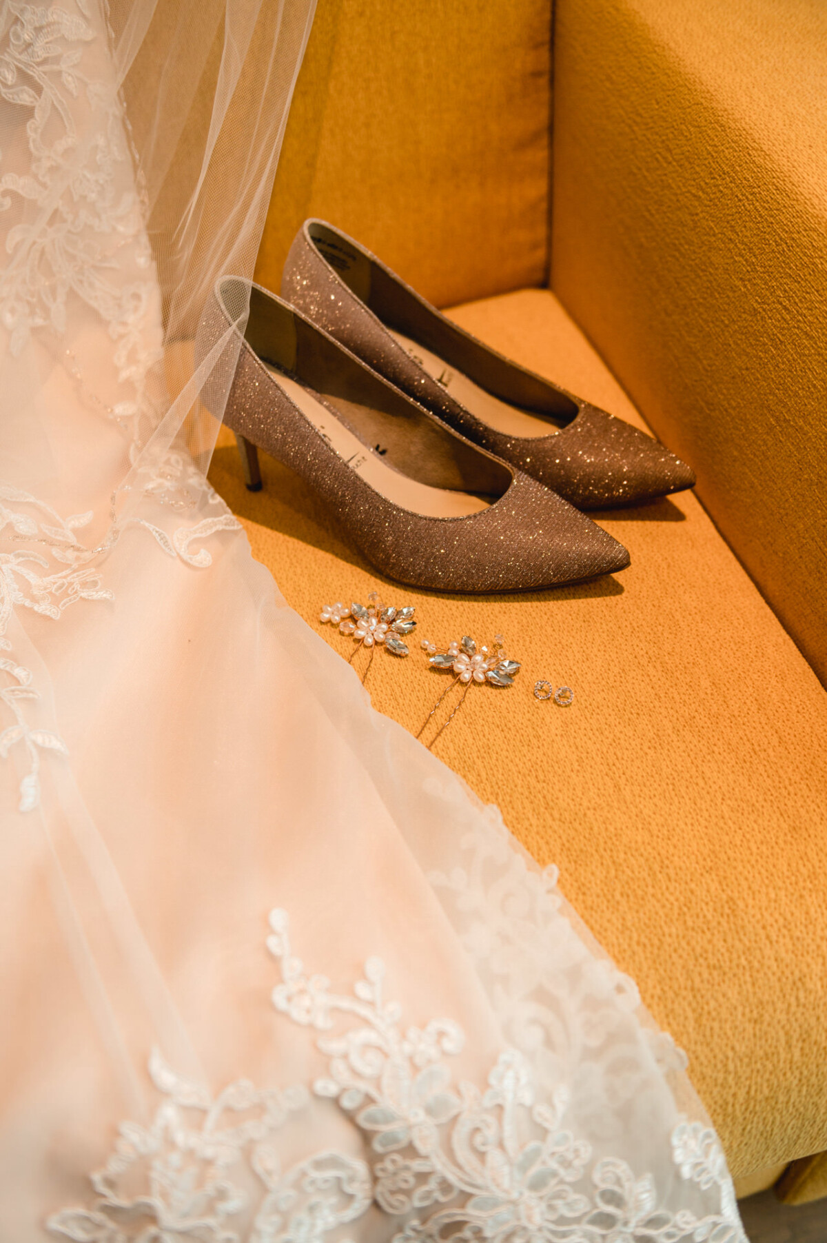 christian-lorenz.net Ein Paar glitzernde High Heels, Perlenohrringe und ein Spitzenschleier auf einem orangefarbenen Sofa.