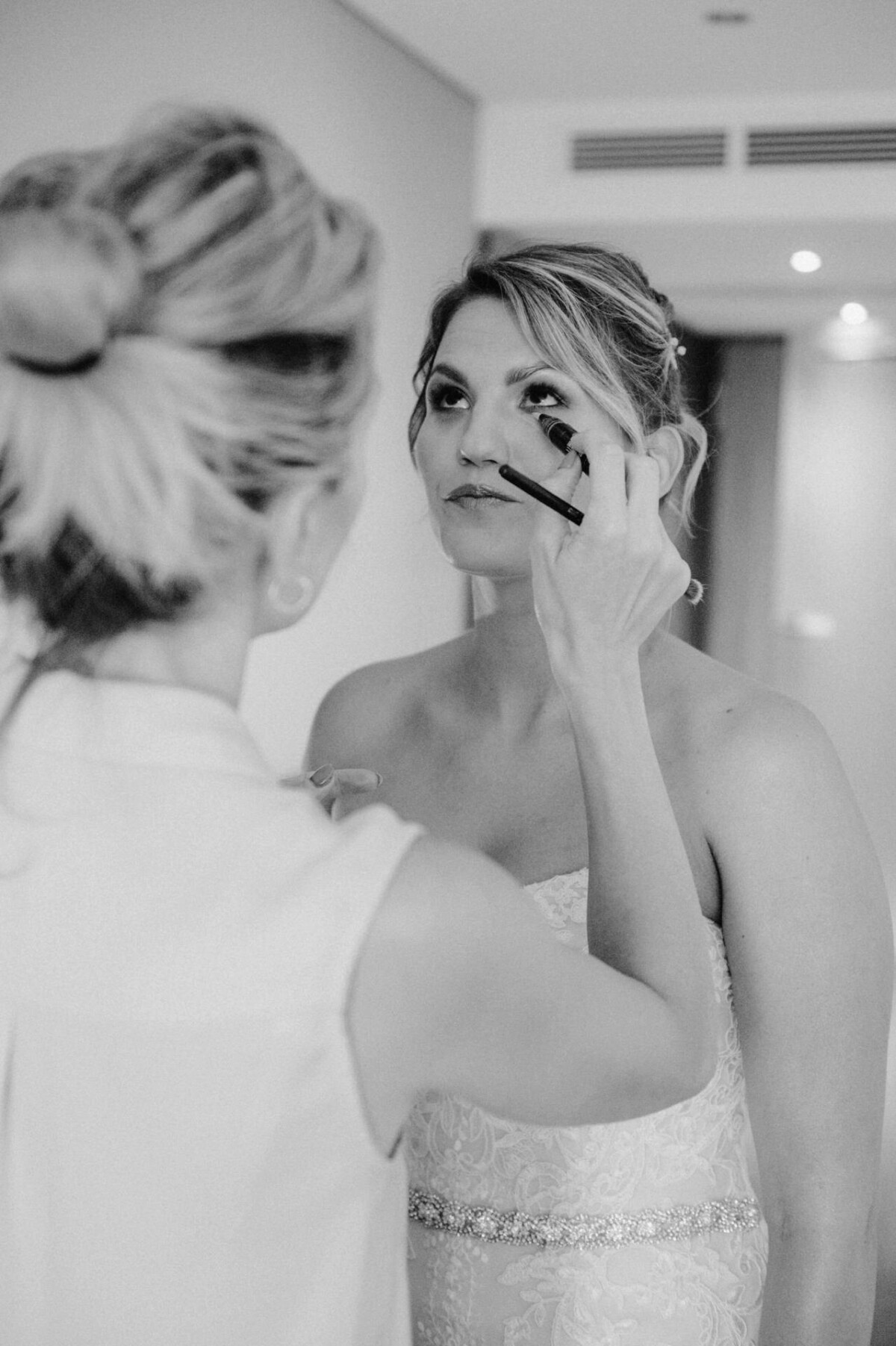 christian-lorenz.net Eine Frau im trägerlosen Kleid lässt sich von einer anderen Frau im ärmellosen Top schminken.