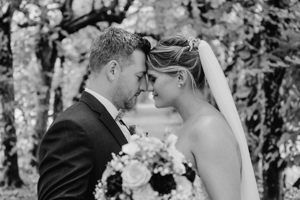 christian-lorenz.net Braut und Bräutigam stehen Stirn an Stirn in einem Wald und halten einen Blumenstrauß.