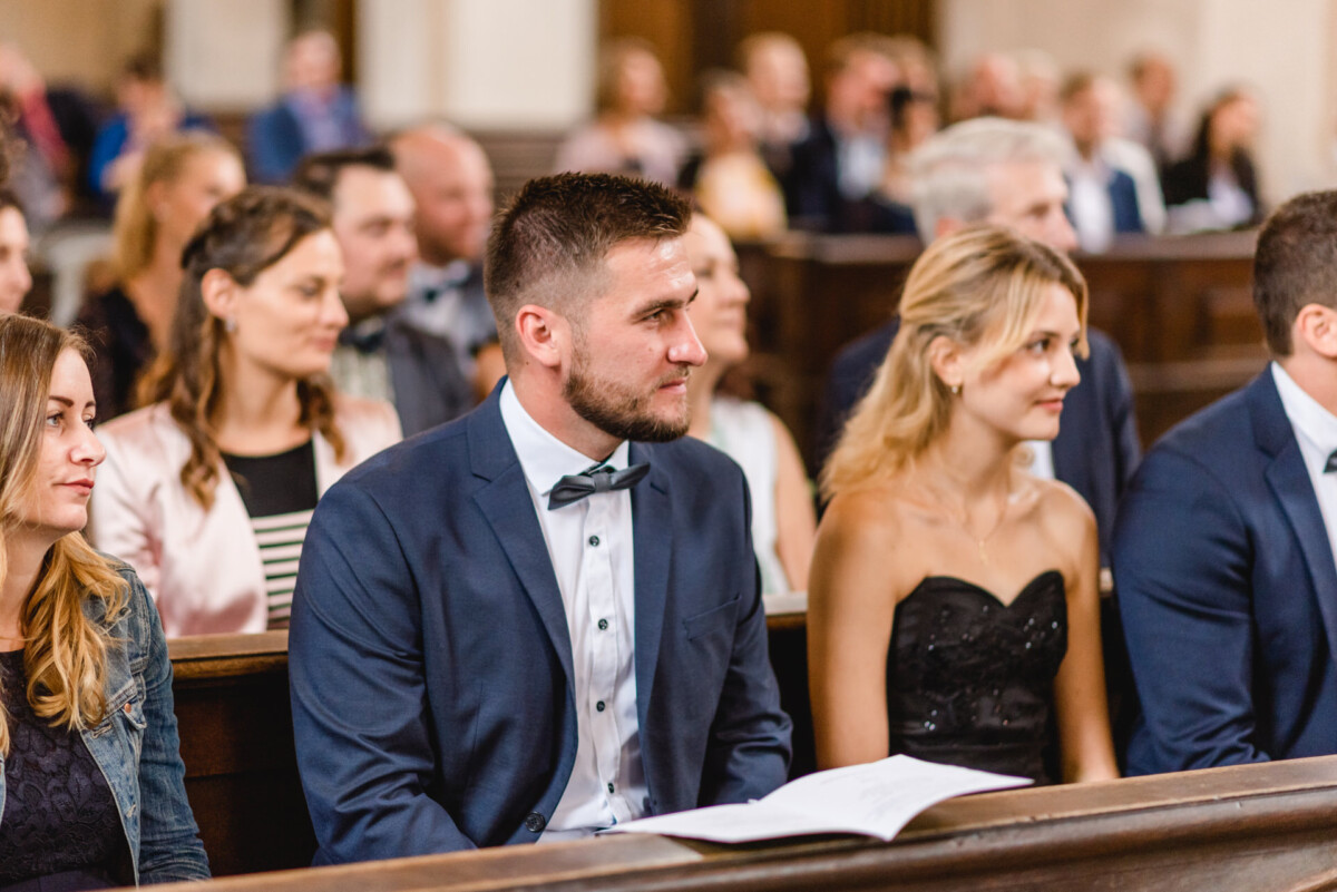 christian-lorenz.net Personen, die in einer Kirche sitzen, formell gekleidet sind und den Anschein erwecken, als würden sie einer Zeremonie oder Veranstaltung beiwohnen.