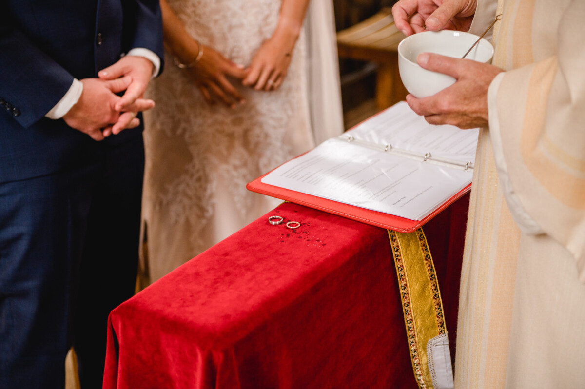 christian-lorenz.net Ein Paar steht neben einem Priester, der eine Schale hält. Auf einem mit rotem Tuch bedeckten Tisch liegen Eheringe und ein Ordner.