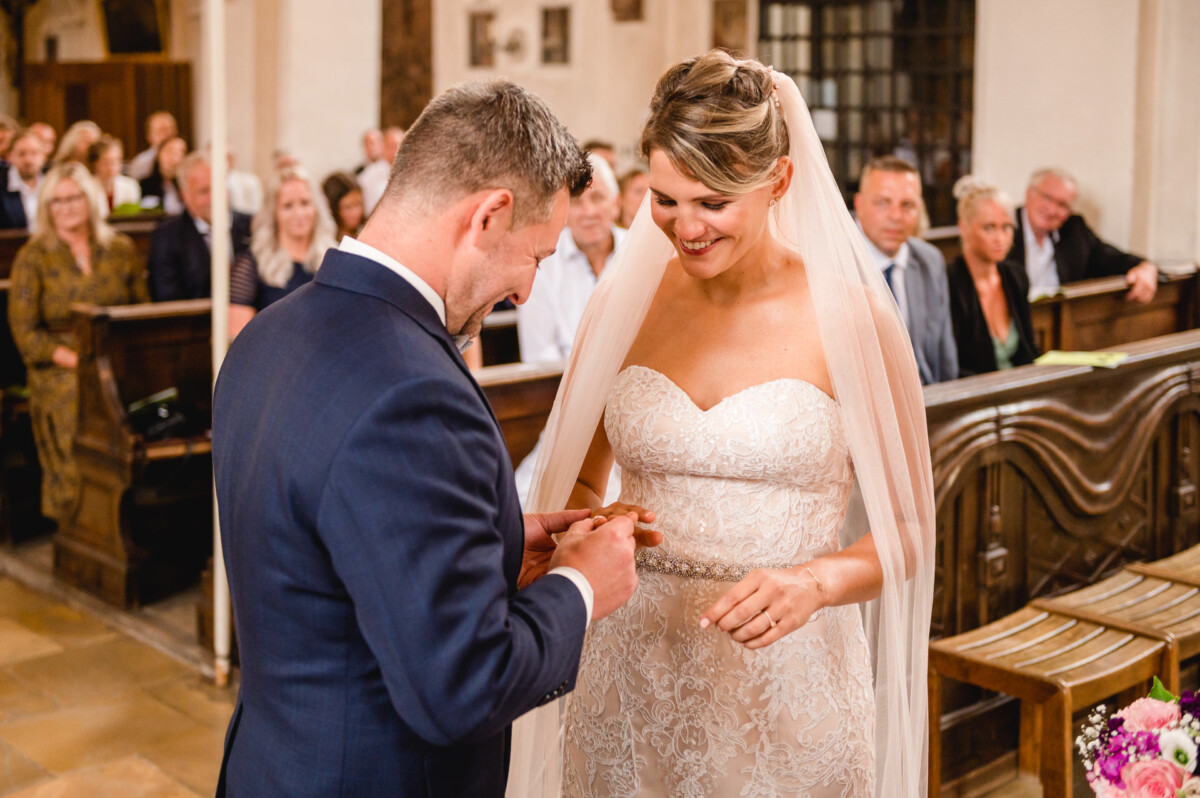 christian-lorenz.net Ein Brautpaar in Abendgarderobe tauscht während einer Hochzeitszeremonie in einer Kapelle Ringe aus, im Hintergrund sitzende Gäste.
