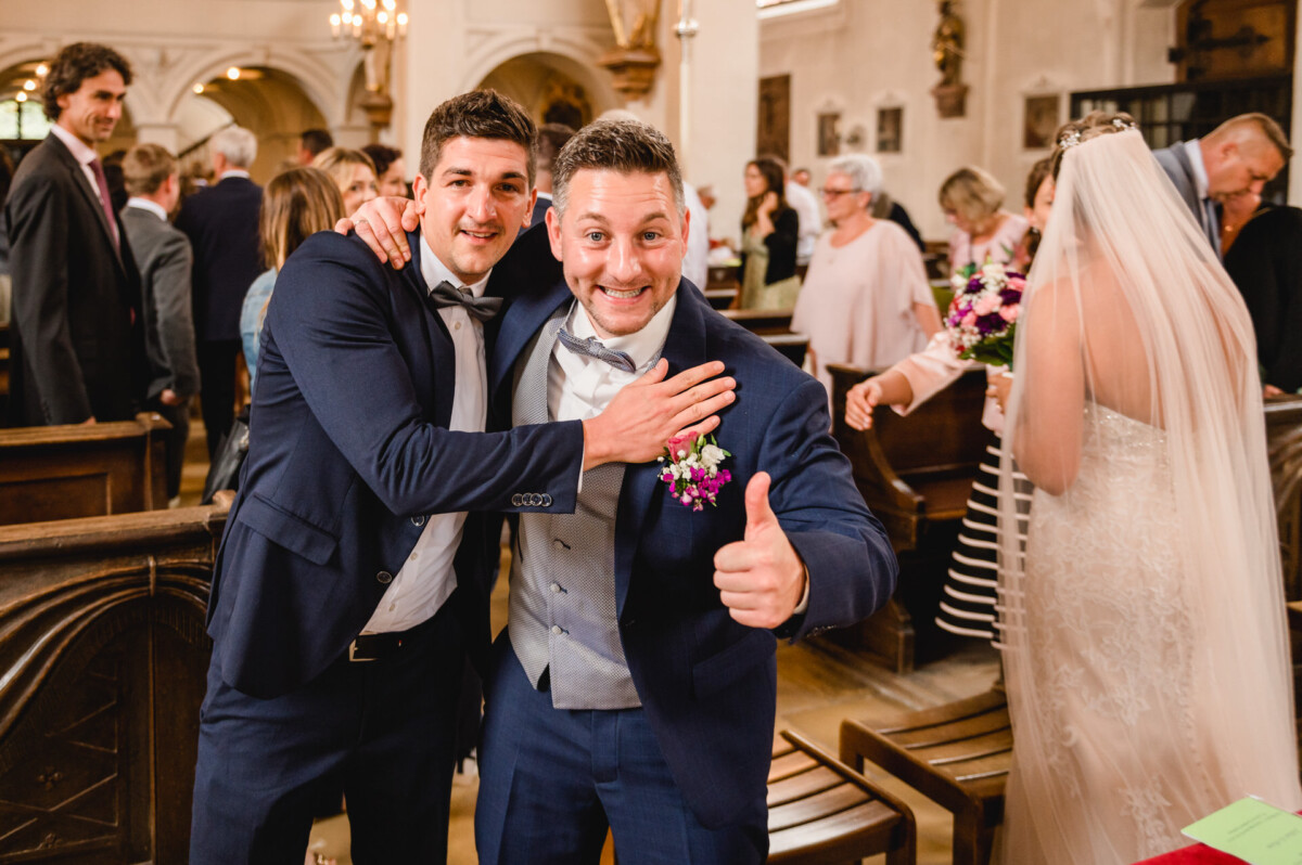 christian-lorenz.net Zwei Männer in Anzügen lächeln, einer zeigt den Daumen nach oben, in einem überfüllten Veranstaltungsort mit Menschen in Abendgarderobe.