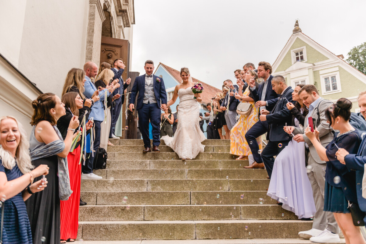 christian-lorenz.net Ein Brautpaar geht umgeben von Gästen die Treppe hinunter. Die Gäste pusten Seifenblasen und klatschen jubelnd.