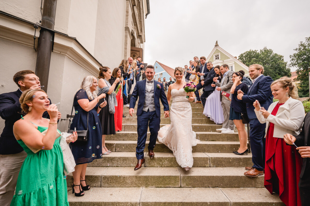 christian-lorenz.net Ein Brautpaar steigt, umgeben von Gästen, die zur Feier des Tages Seifenblasen pusten, die Außentreppe hinunter.